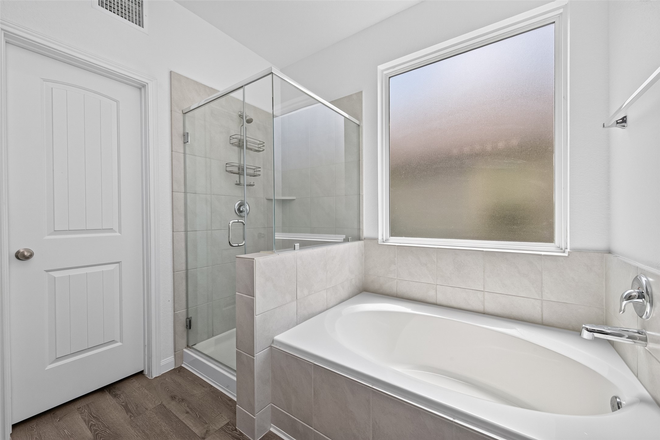 2526 Sturgeon Way Conroe, TX 77384 - Photo 22 of 49 This bathroom features a modern design with a glass-enclosed shower and a spacious bathtub. It has a frosted window for privacy, neutral tile walls, and wood-look flooring, creating a clean and inviting space.