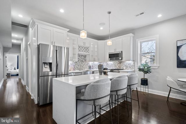 a kitchen with stainless steel appliances granite countertop a refrigerator a stove a sink a dining table and chairs with wooden floor