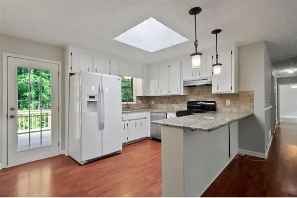 a kitchen with stainless steel appliances granite countertop a refrigerator a sink dishwasher a stove a refrigerator and white cabinets with wooden floor