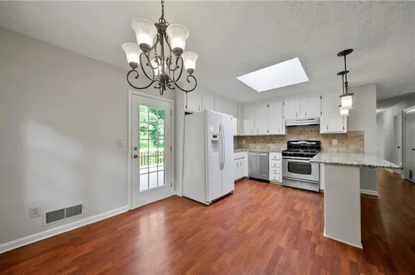 a kitchen with stainless steel appliances granite countertop a refrigerator a stove top oven a sink dishwasher and white cabinets with wooden floor