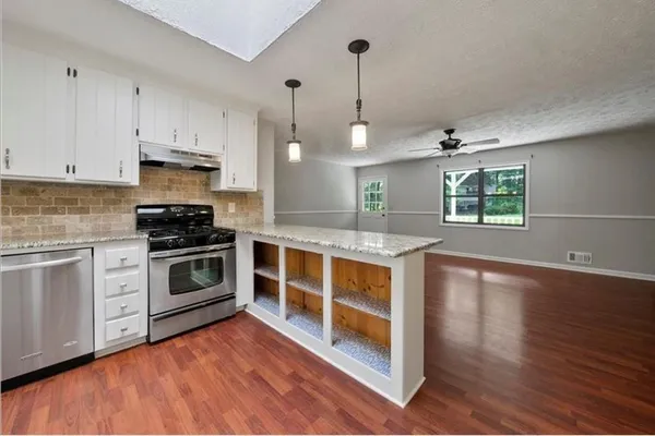 a kitchen with kitchen island granite countertop a stove a sink and white cabinets with wooden floor