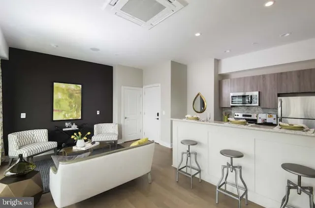 a living room with stainless steel appliances furniture a rug and a view of kitchen