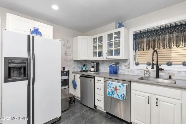 a kitchen with a refrigerator a sink and dishwasher with white cabinets
