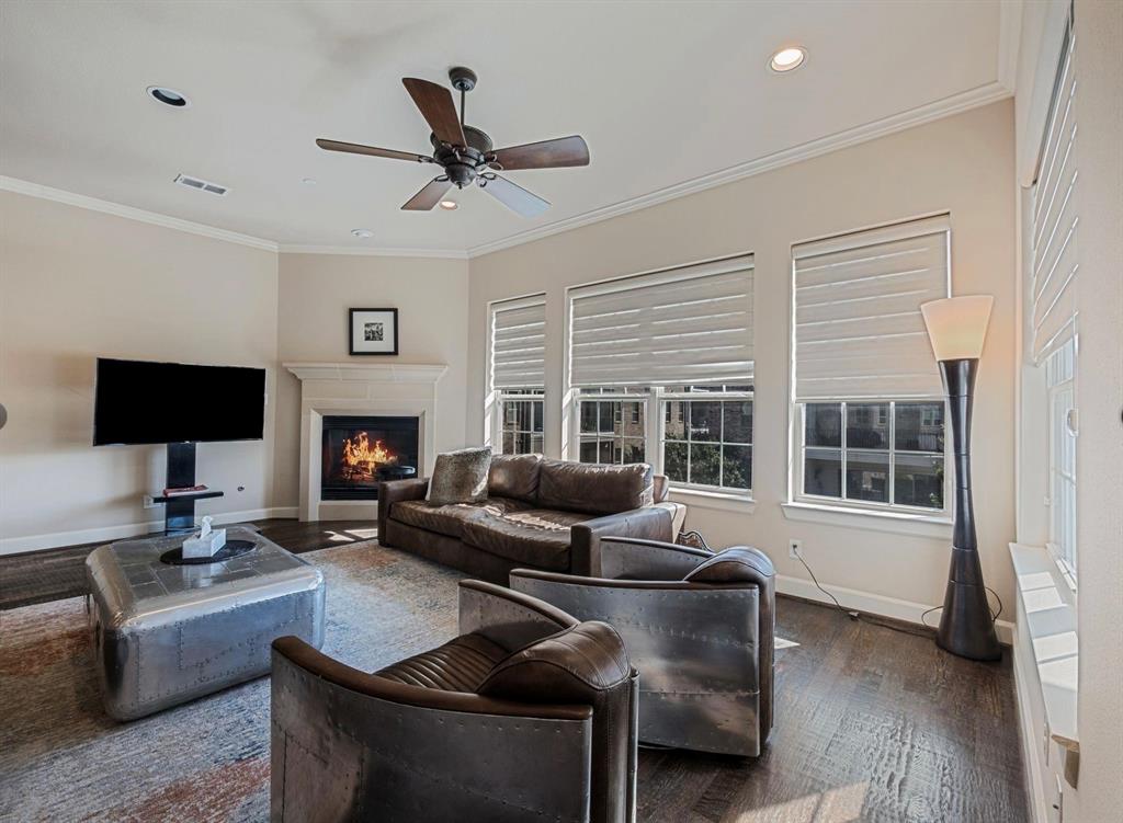 5001 Meridian Lane, Unit 2103 Addison, TX 75001 - Photo 2 of 26 Living area featuring wood-finish flooring, a corner fireplace with a stone mantel, multiple windows with blinds, a ceiling fan, and recessed lighting