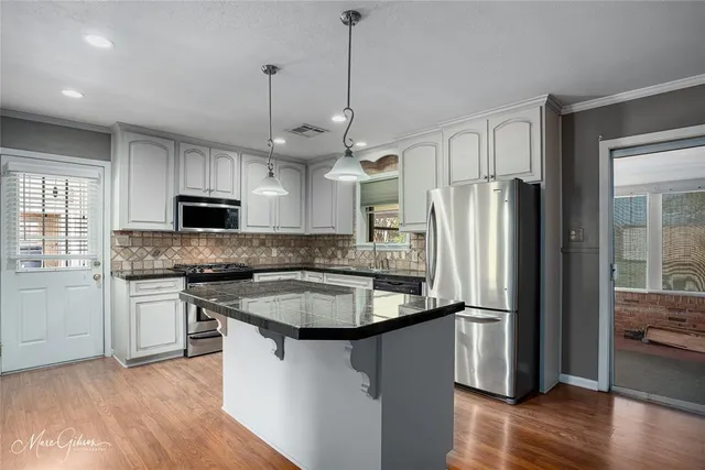 a kitchen with stainless steel appliances granite countertop a refrigerator a sink dishwasher a stove and white cabinets with wooden floor