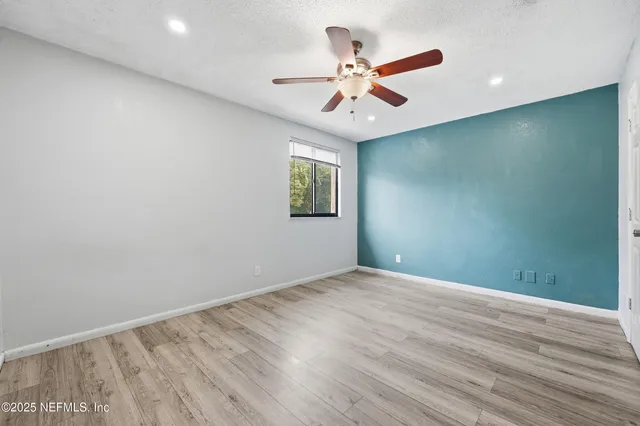 an empty room with wooden floor fan and windows