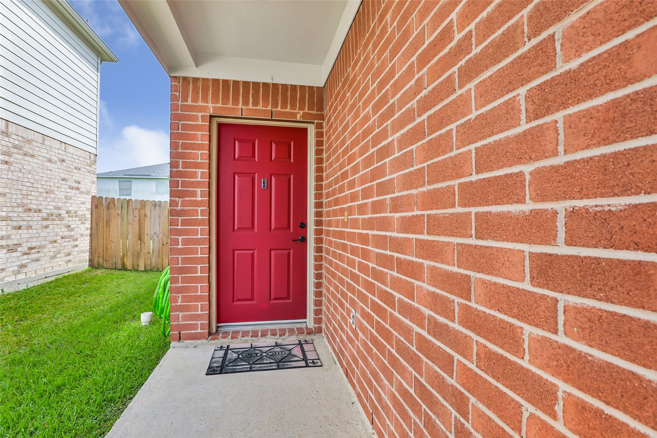 12122 Landsdown Ridge Way Humble, TX 77346 - Photo 7 of 34 This photo showcases a welcoming entrance with a bold red door set in a brick exterior. The entryway is covered and features a neatly maintained lawn and a wooden fence for privacy.