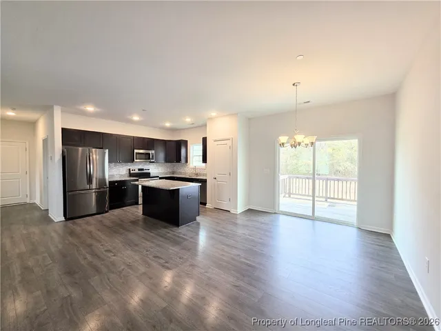 a kitchen with stainless steel appliances kitchen island granite countertop a refrigerator a sink a stove and white cabinets with wooden floor