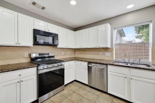 a kitchen with granite countertop white cabinets appliances a sink and a window