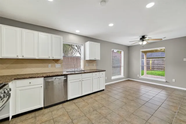 a open kitchen with granite countertop a sink and dishwasher a stove top oven with white cabinets