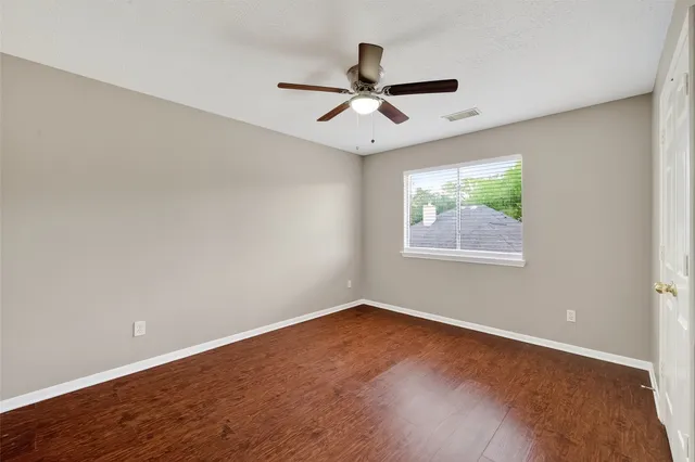 an empty room with wooden floor ceiling fan and windows