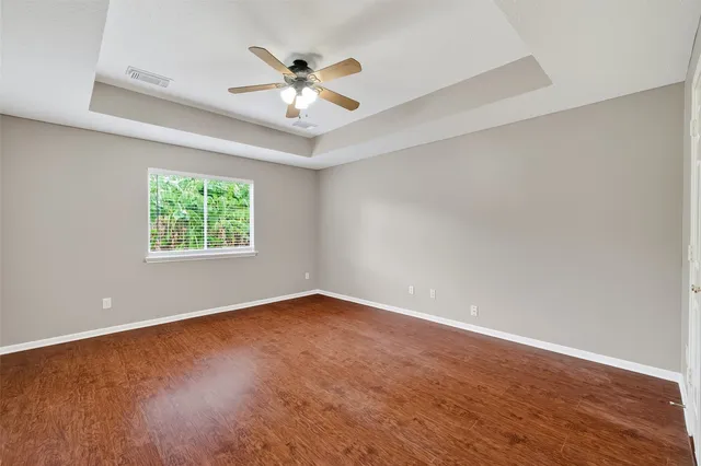 an empty room with wooden floor chandelier fan and windows