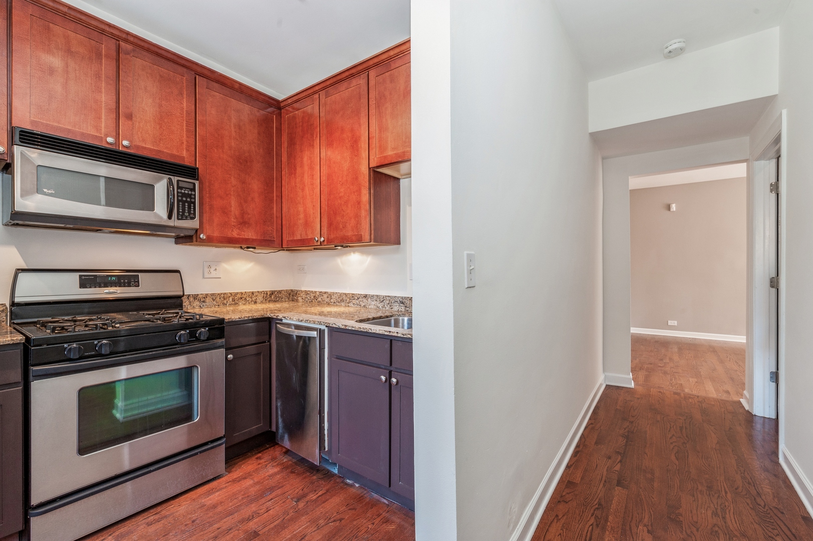 5743 North Ridge Avenue, Unit 1 Chicago, IL 60660 - Photo 7 of 12 a kitchen with granite countertop wooden cabinets stainless steel appliances and a wooden floor