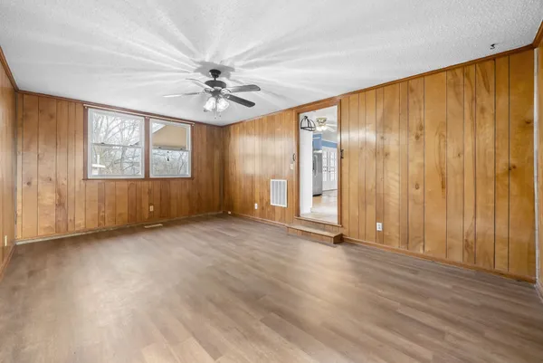 an empty room with wooden floor chandelier fan and windows