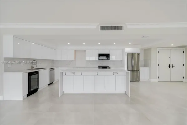 a large white kitchen with stainless steel appliances kitchen island granite countertop a stove a sink a refrigerator and white cabinets