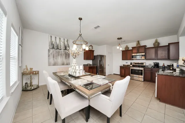 a kitchen with granite countertop stainless steel appliances a sink dishwasher a stove a refrigerator a dining table and chairs with wooden floor