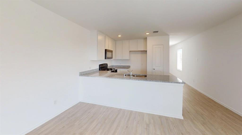 9757 Platteview Road Fort Worth, TX 76179 - Photo 3 of 19 Kitchen featuring white cabinetry, light-toned wood-finish flooring, a stainless steel sink, granite-style countertops, and a built-in microwave