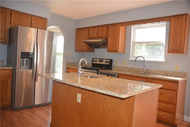 a kitchen with stainless steel appliances granite countertop a refrigerator a sink a stove a washer and dryer with wooden floor