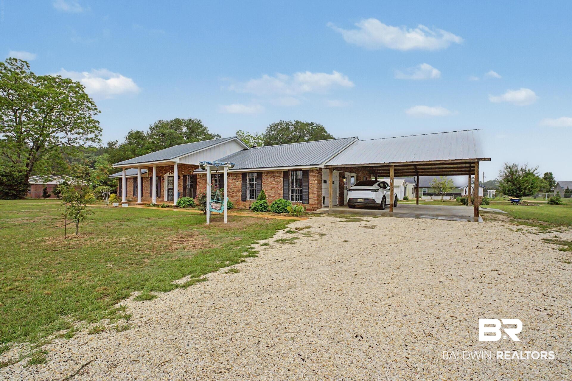 3791 Robinsonville Road Atmore, AL 36502 - Photo 5 of 47 Brick exterior with a metal roof, featuring a covered front porch with white columns, dark shutters, and an attached two-car carport