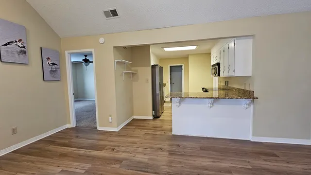an empty room with wooden floor and way to kitchen
