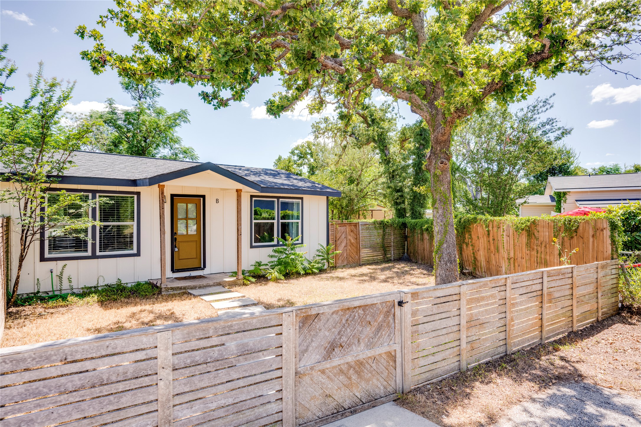 1400 Marcus Place, Unit B Austin, TX 78721 - Photo 8 of 39 A charming single-story home with a golden entry door, set behind a rustic wooden fence and gate.