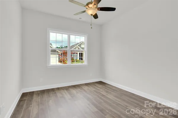 an empty room with wooden floor chandelier fan and windows