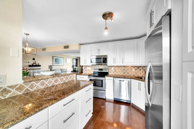 a kitchen with stainless steel appliances granite countertop a refrigerator a stove a sink and white cabinets with wooden floor