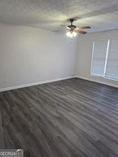 a view of an empty room with wooden floor and a ceiling fan