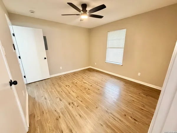 a view of an empty room with wooden floor and a ceiling fan