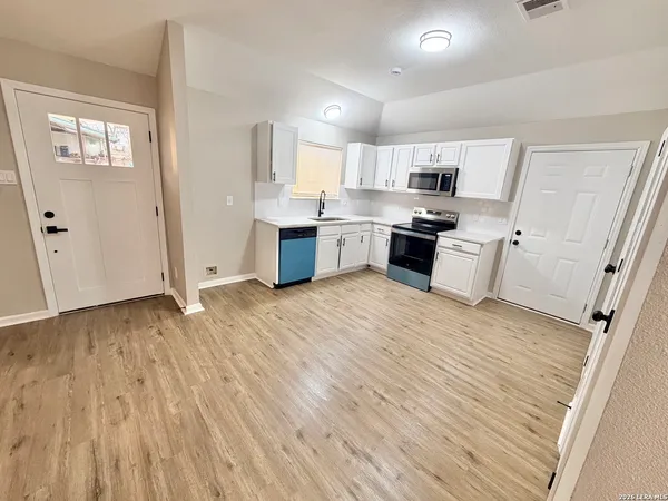 a large white kitchen with stainless steel appliances wooden floors and white walls