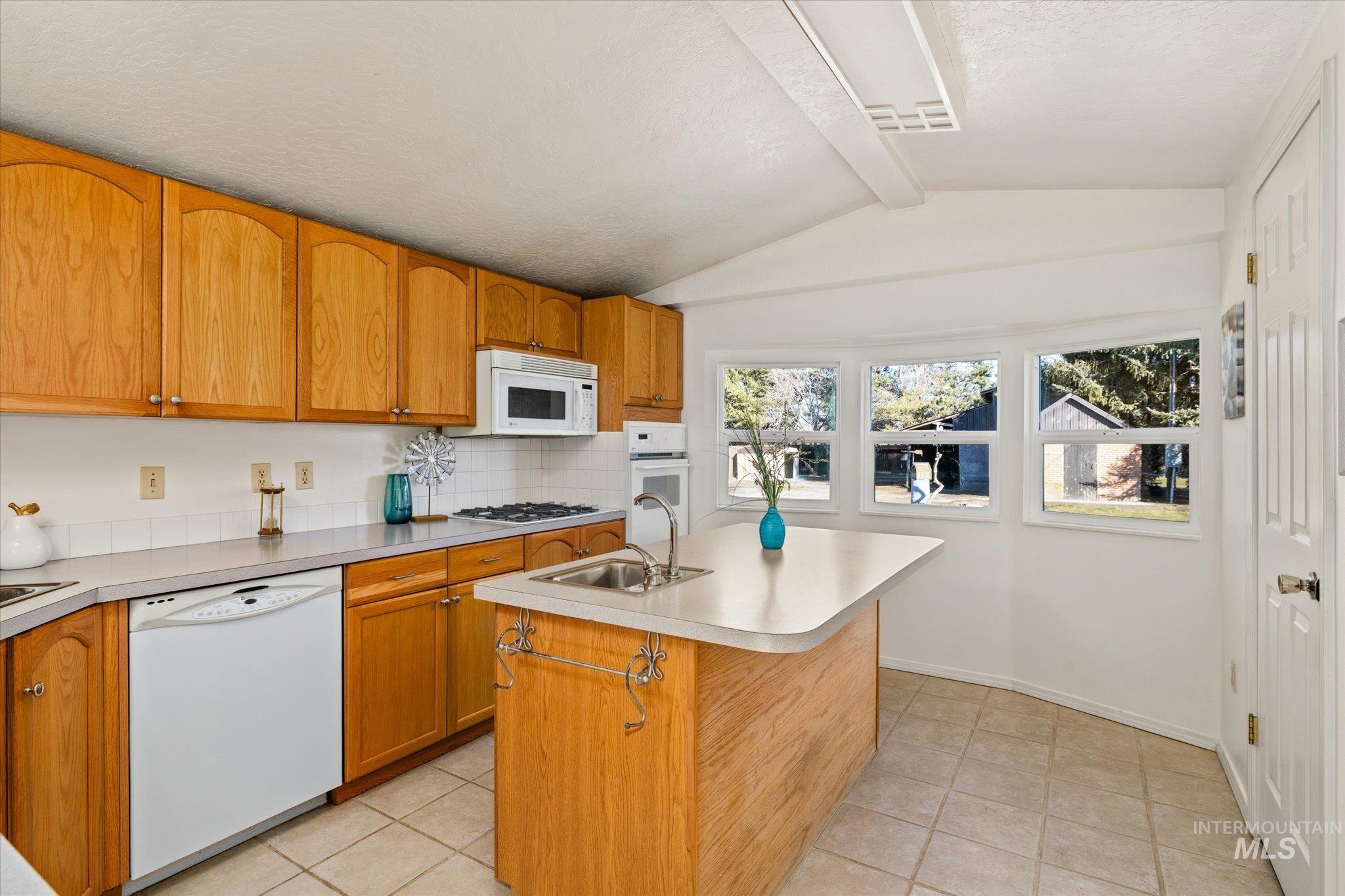 9820 Highway 44 Middleton, ID 83644 - Photo 22 of 50 Kitchen featuring white appliances, an island with sink, backsplash, light countertops, and light tile patterned floors
