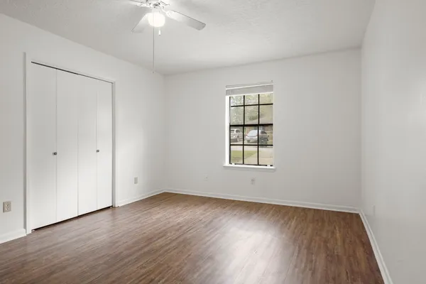 an empty room with wooden floor chandelier fan and windows