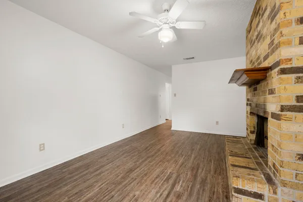 an empty room with wooden floor fan and windows