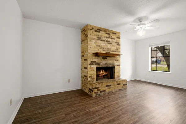 a view of an empty room with wooden floor fireplace and a window