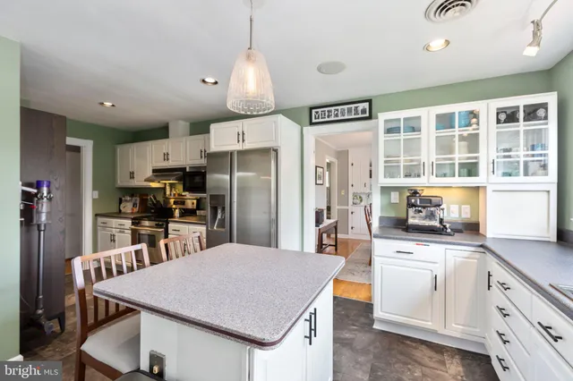 a kitchen with stainless steel appliances kitchen island granite countertop a refrigerator a sink a stove and white cabinets with wooden floor