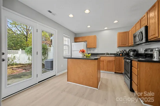 a kitchen with stainless steel appliances granite countertop a refrigerator a sink dishwasher a stove and a dining table with wooden floor