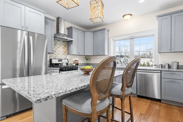 a kitchen with stainless steel appliances granite countertop a stove a refrigerator a sink dishwasher a dining table and chairs with wooden floor