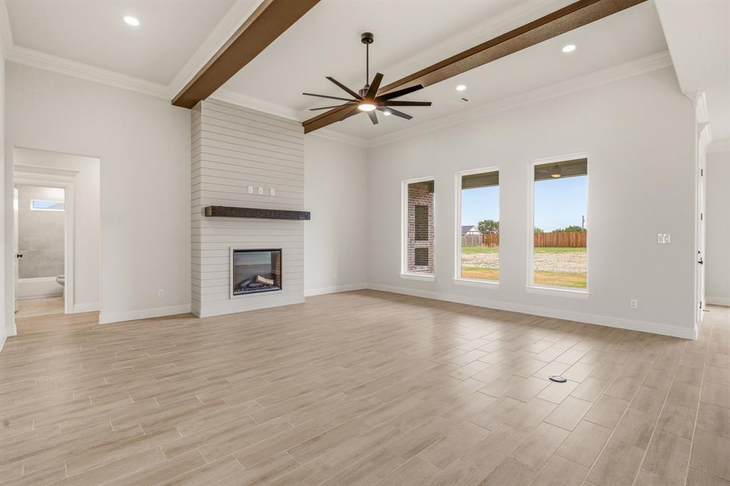 3155 Infinity Drive Weatherford, TX 76087 - Photo 8 of 39 Unfurnished living room featuring a ceiling fan, a large fireplace, healthy amount of natural light, ornamental molding, and wood finish floors