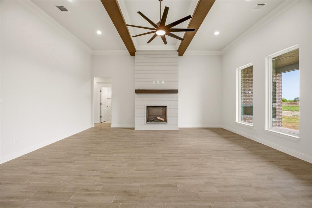 3155 Infinity Drive Weatherford, TX 76087 - Photo 9 of 39 Unfurnished living room with ceiling fan, a large fireplace, wood tiled floors, crown molding, and beam ceiling