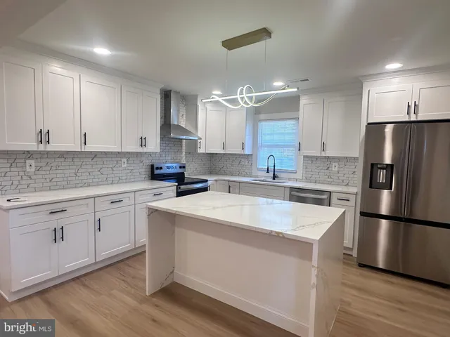 a kitchen with stainless steel appliances granite countertop a refrigerator a sink dishwasher a stove and white cabinets with wooden floor