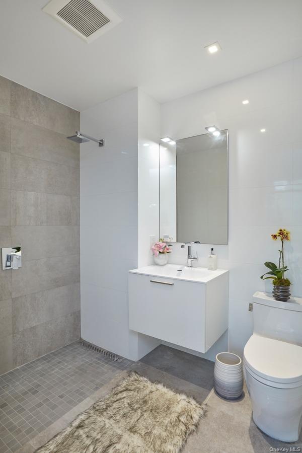 24-12 42nd Road, Unit 6C Queens, NY 11101 - Photo 7 of 12 a bathroom with a sink a toilet and a mirror