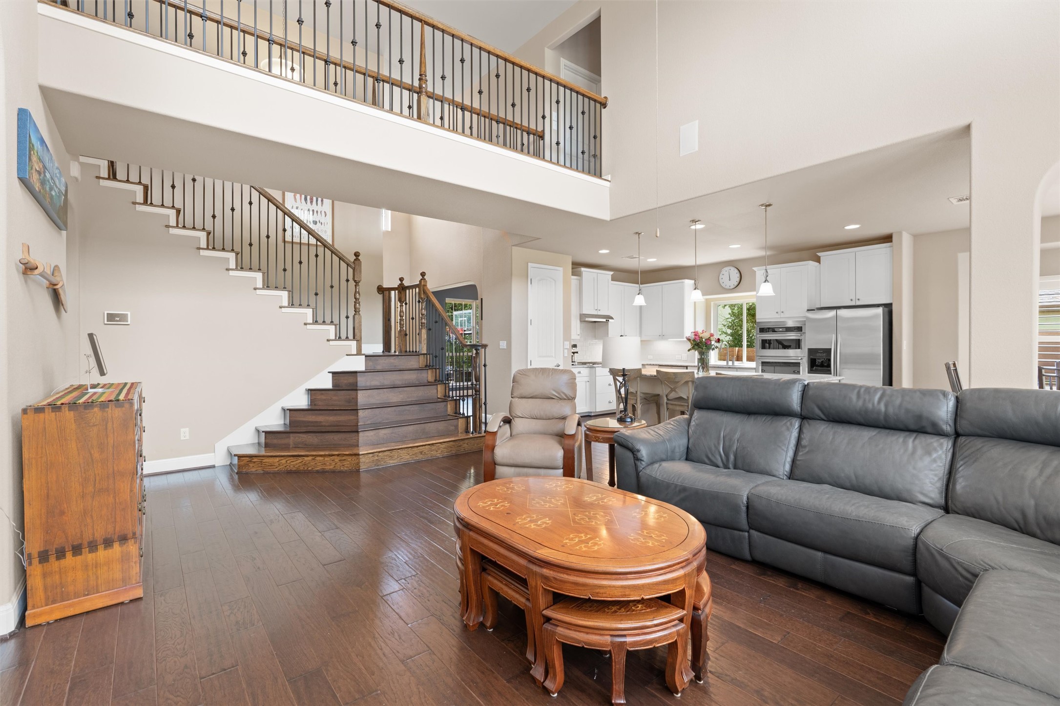 7716 Aria Loop Austin, TX 78736 - Photo 10 of 39 A spacious, open-concept living area unfolds with gleaming hardwood floors and a striking staircase leading to an upper-level balcony.
