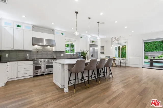 a kitchen with stainless steel appliances granite countertop a stove top oven a sink dishwasher a dining table and chairs with wooden floor