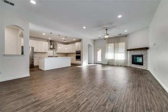 a view of an empty room and kitchen with wooden floor