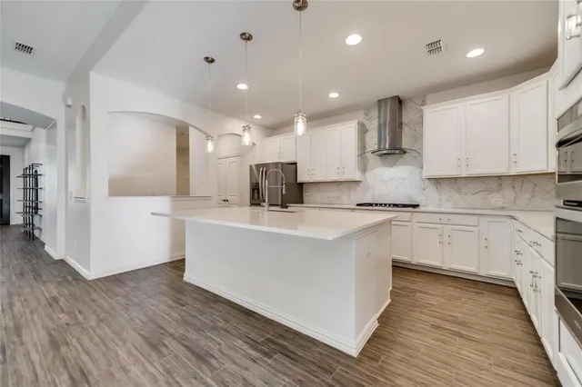 a large white kitchen with kitchen island a sink a stove a refrigerator and white cabinets with wooden floor