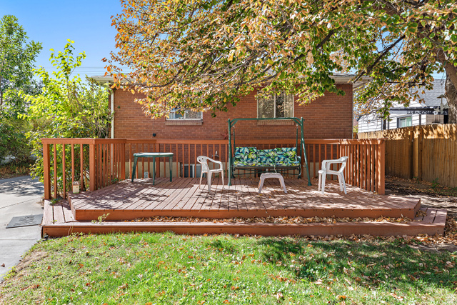 664 Wasatch Street Midvale, UT 84047 - Photo 20 of 33 Expansive outdoor deck with wood-finish railing and steps, set against a brick exterior, and surrounded by mature trees