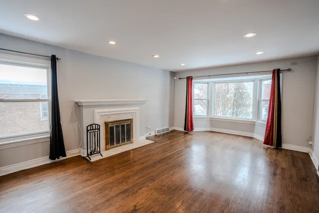 an empty room with wooden floor fireplace and windows