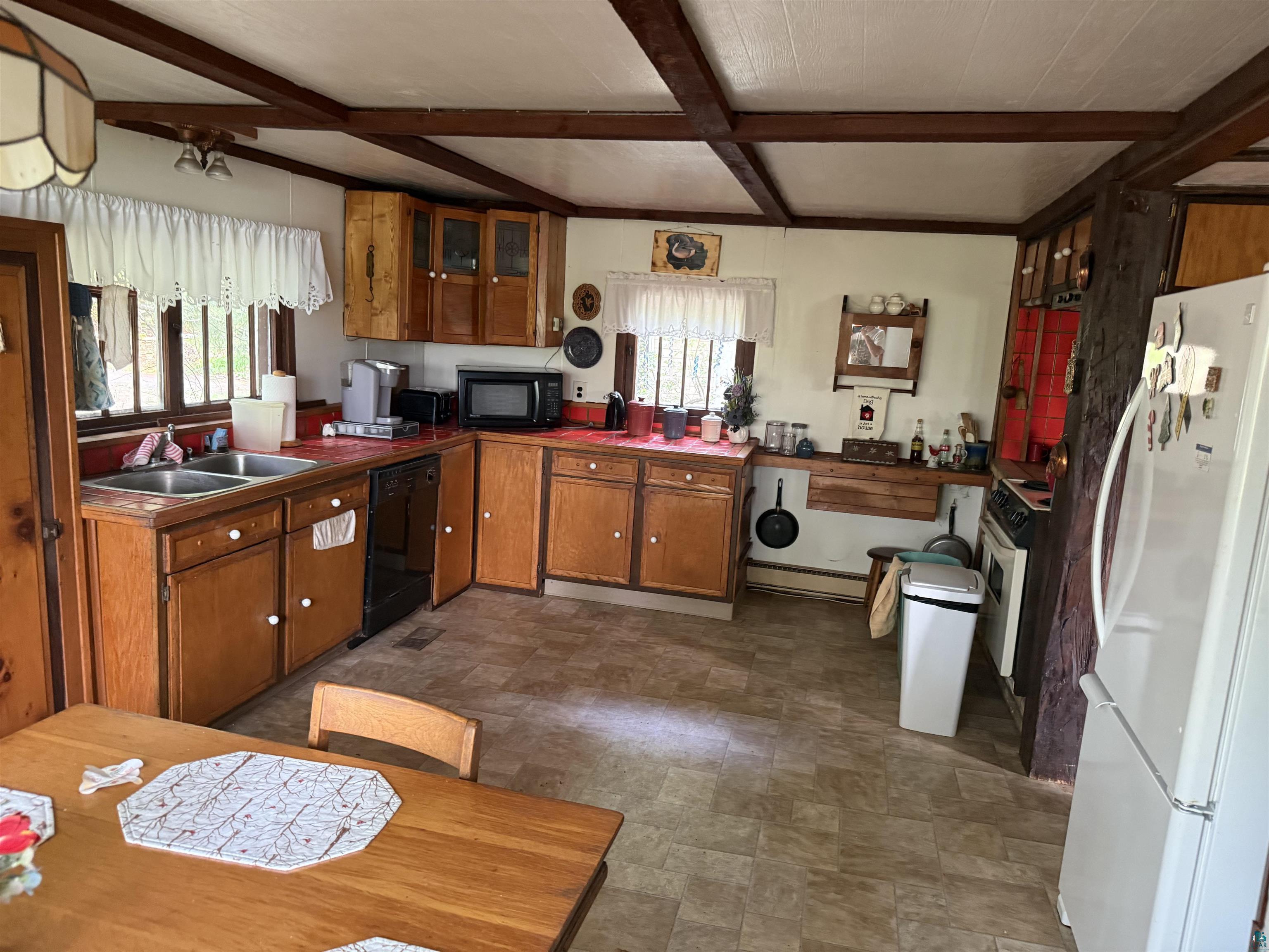 69175 East Long Lake Road Iron River, WI 54847 - Photo 10 of 47 Kitchen featuring black appliances, a sink, brown cabinets, beamed ceiling, and a baseboard radiator