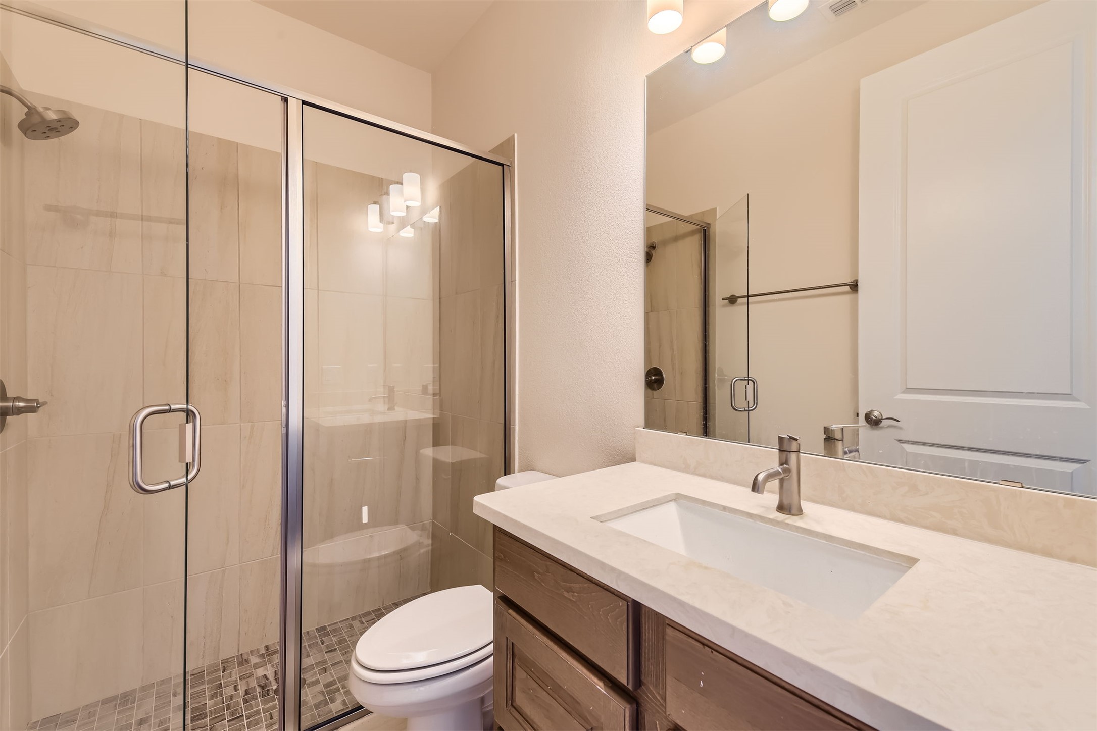 8313 Spire View Austin, TX 78744 - Photo 20 of 33 A well-lit bathroom features a glass-enclosed shower and a vanity with stone counters.