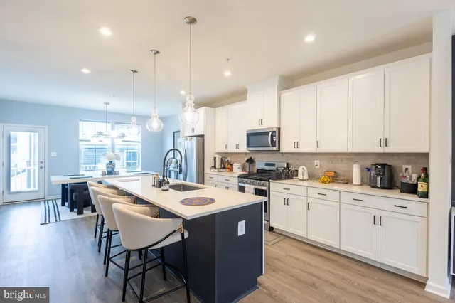 a kitchen with stainless steel appliances kitchen island granite countertop a stove a sink a refrigerator and white cabinets with wooden floor